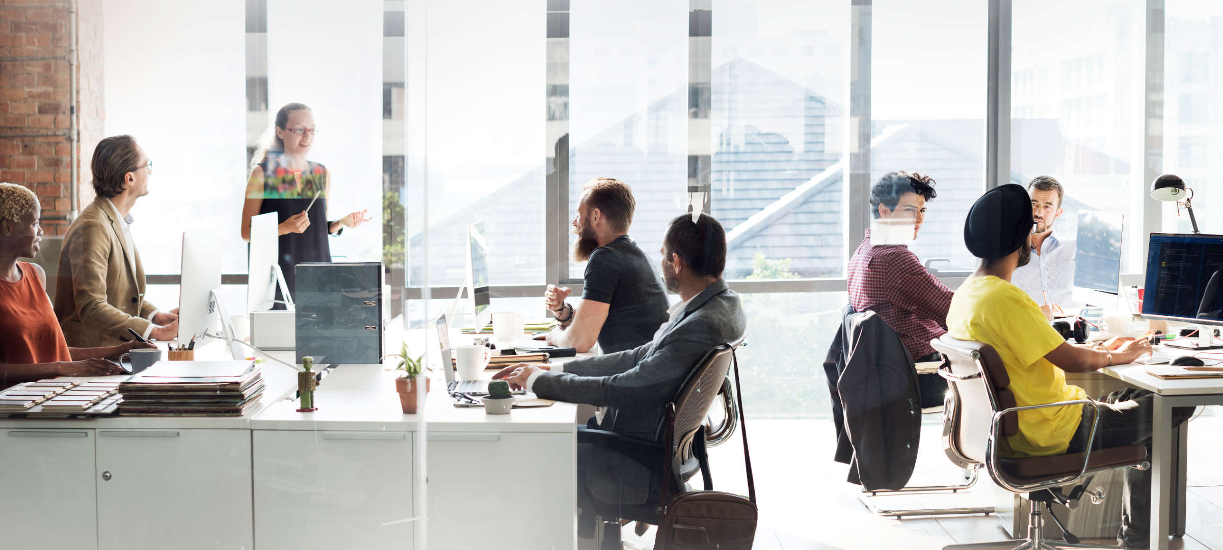 Ein Meeting im Büro einer modernen Agentur für Design in Frankfurt am Main. Im lichtdurchfluteten Office sitzen Designer und Programmierer hinter Tischen an Computern. Sie entwerfen Gestaltung für Online- und Printmedien, programmieren Webdesigns.